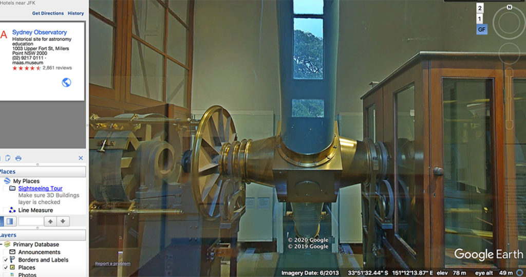 View of central tube of gold and blue telescope with a reflection of a tree from a window